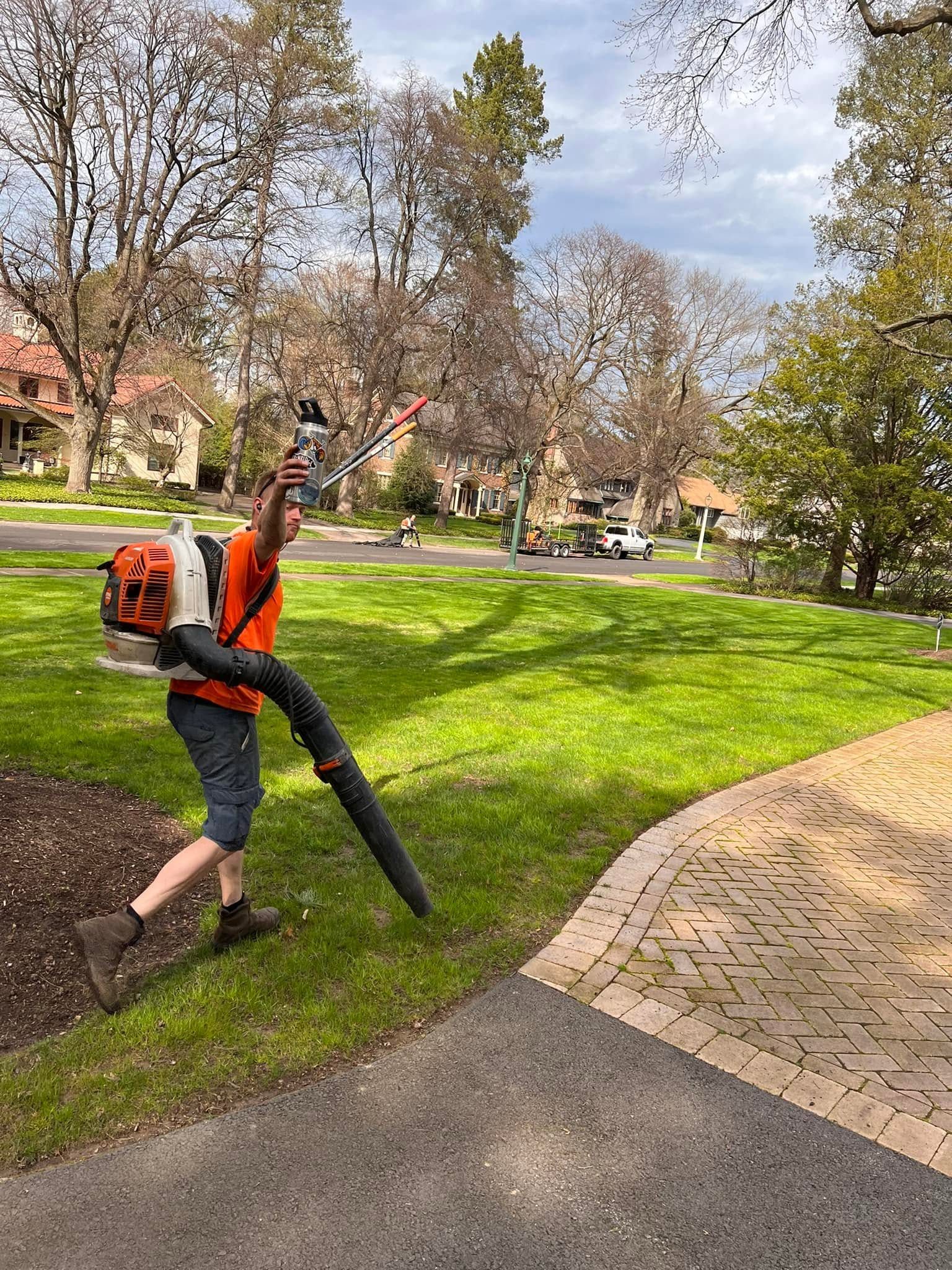 A Cadle's crew member blowing off a manicured lawn in a tree lined neighborhood