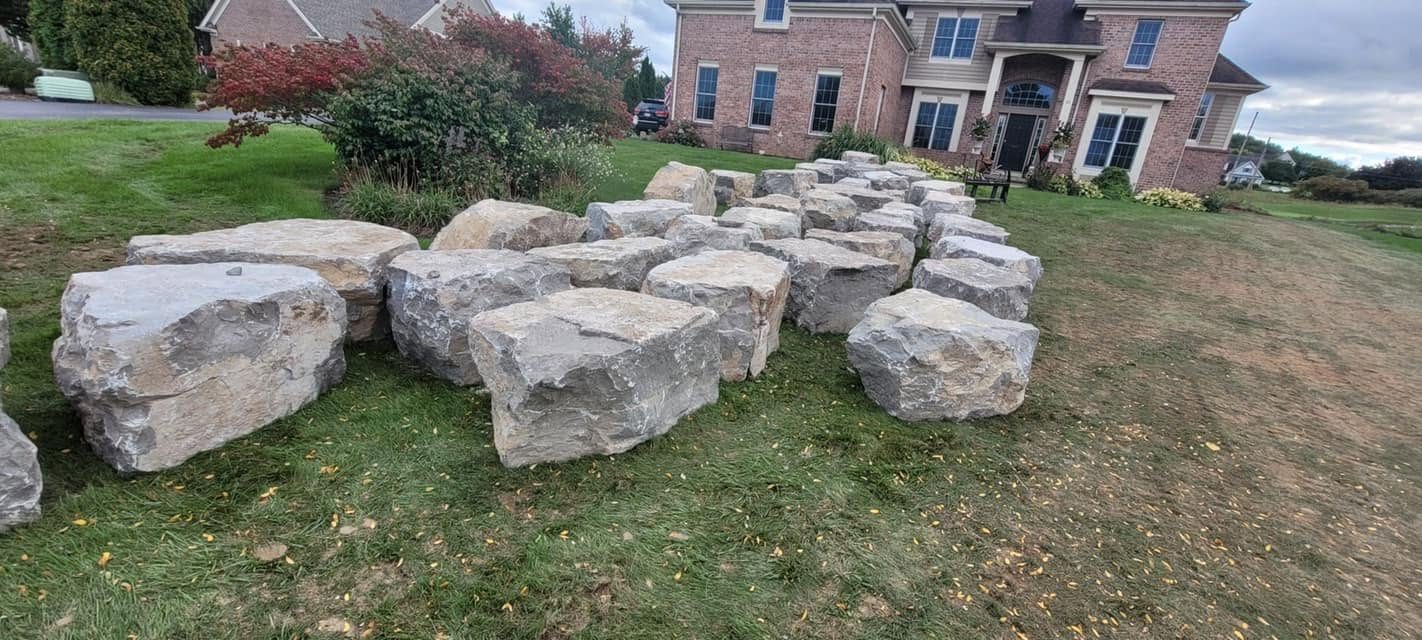 Row of large limestone boulders staged on a lawn in front of a brick home