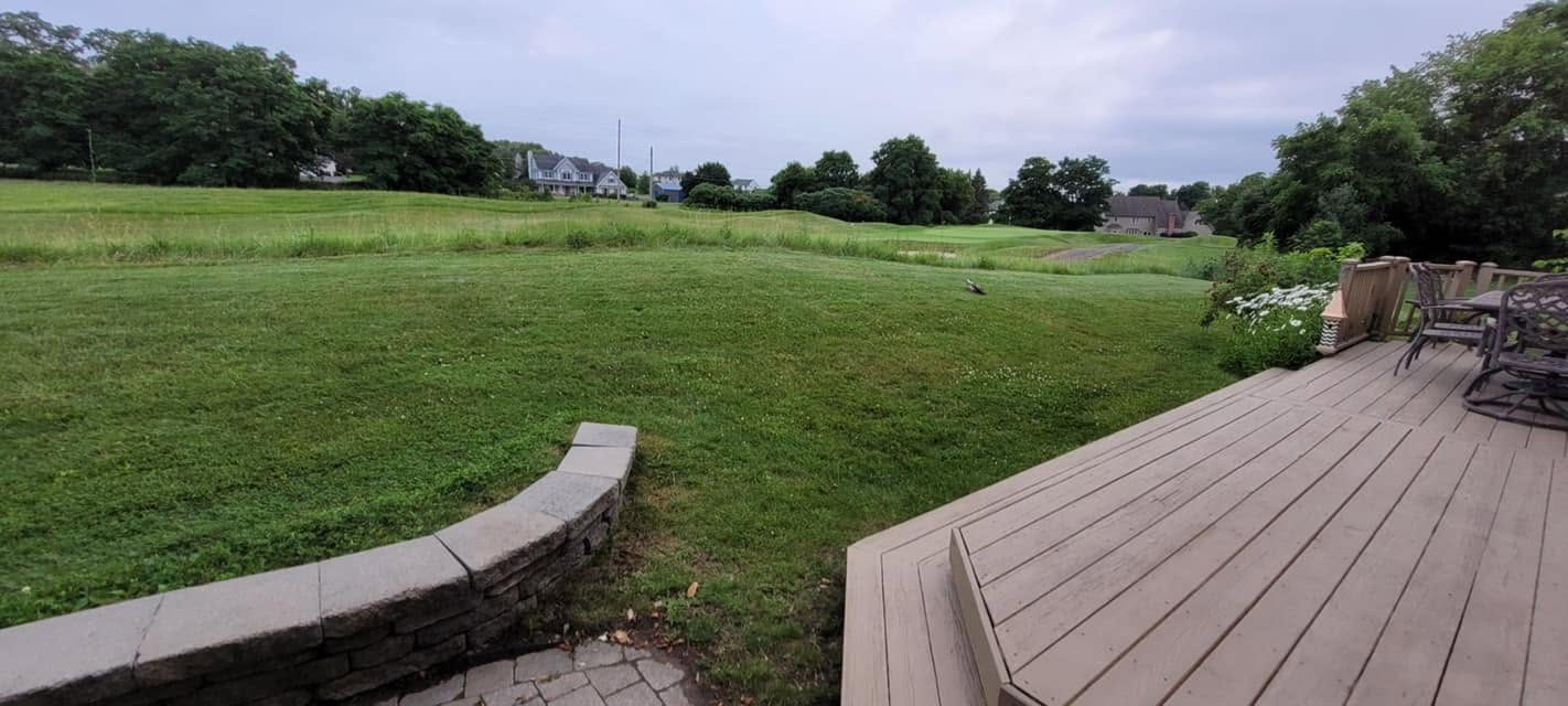 Manicured backyard lawn with a curved stone sitting wall and composite deck