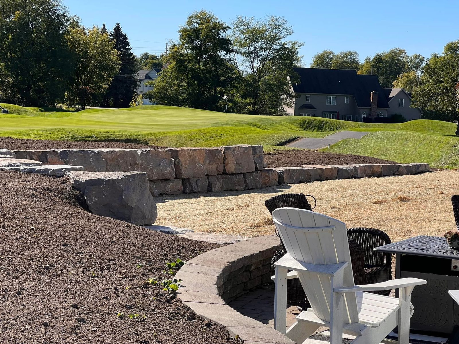 Curved paver patio with seating beside a tiered stone wall overlooking a golf course