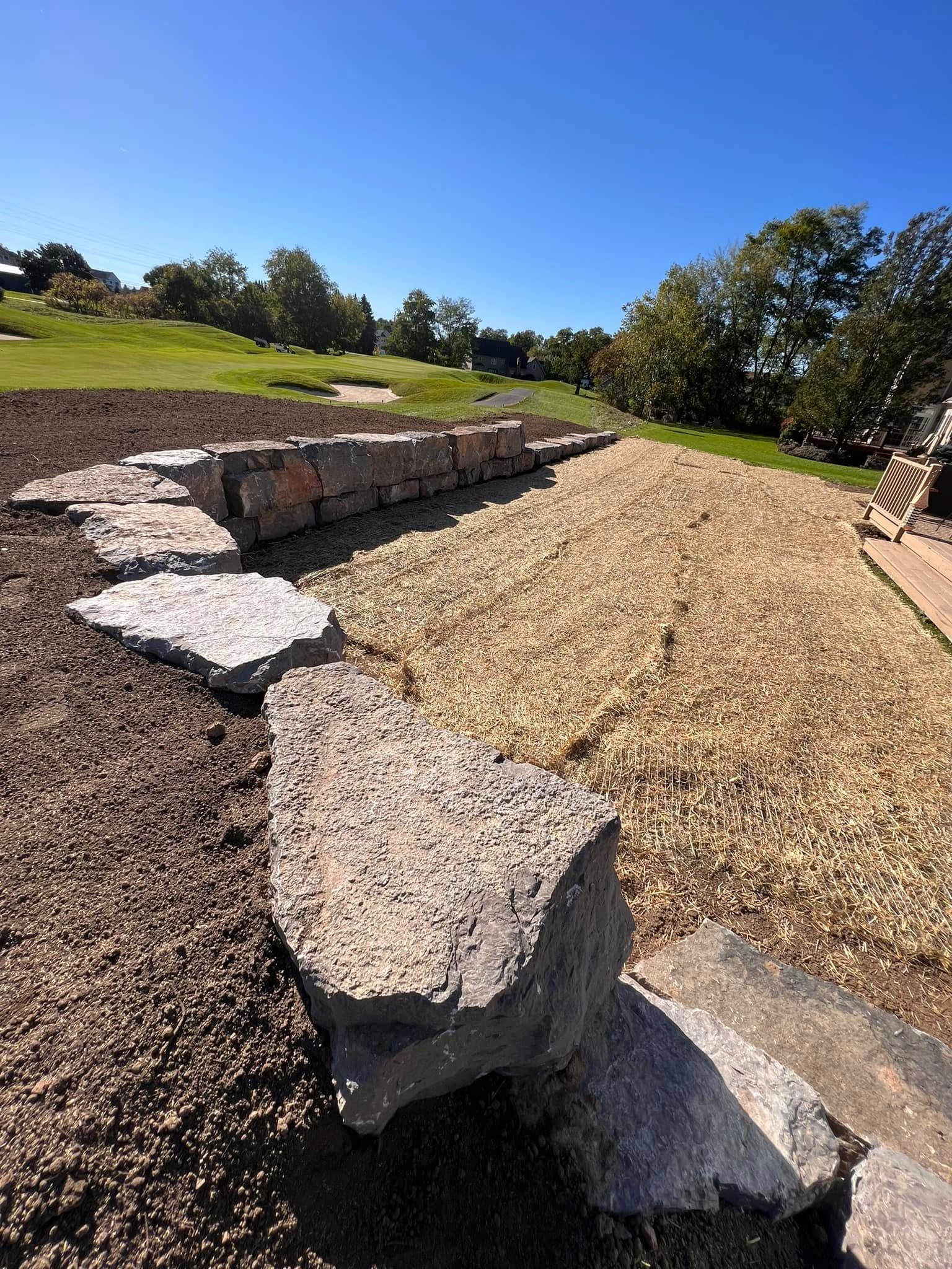Freshly built stone wall beside a newly hydroseeded and strawed lawn area